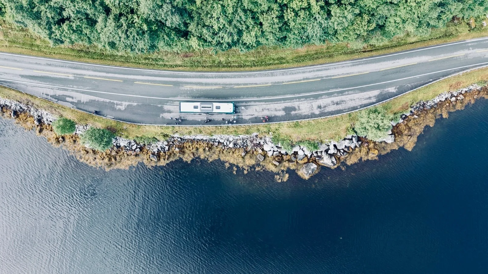 Ein Peters-Reisen Bus hält an einer Straße direkt am Fjord, Luftaufnahme